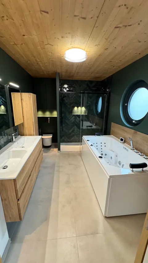Salle de bains aménagée avec baignoire, meubles en bois et hublot
